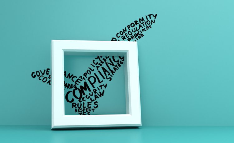 hand drawn check mark on blue wall in front of check box. The check mark is made of Compliance related words: rules, control, governance, respect, law, strategy, conformity, regulation, standards, guide, risk.