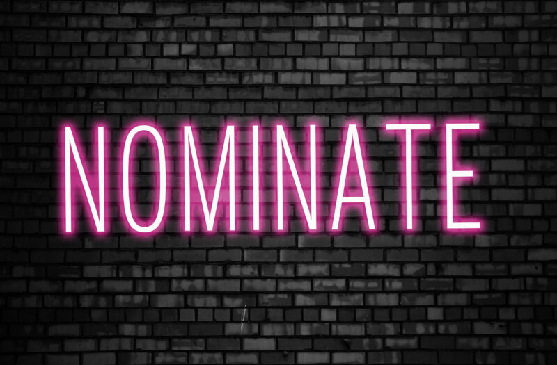 Nominate glowing pink neon sign on black brick wall. Business winner achievement concept for Election Nomination. Image: ANA BARAULIA 